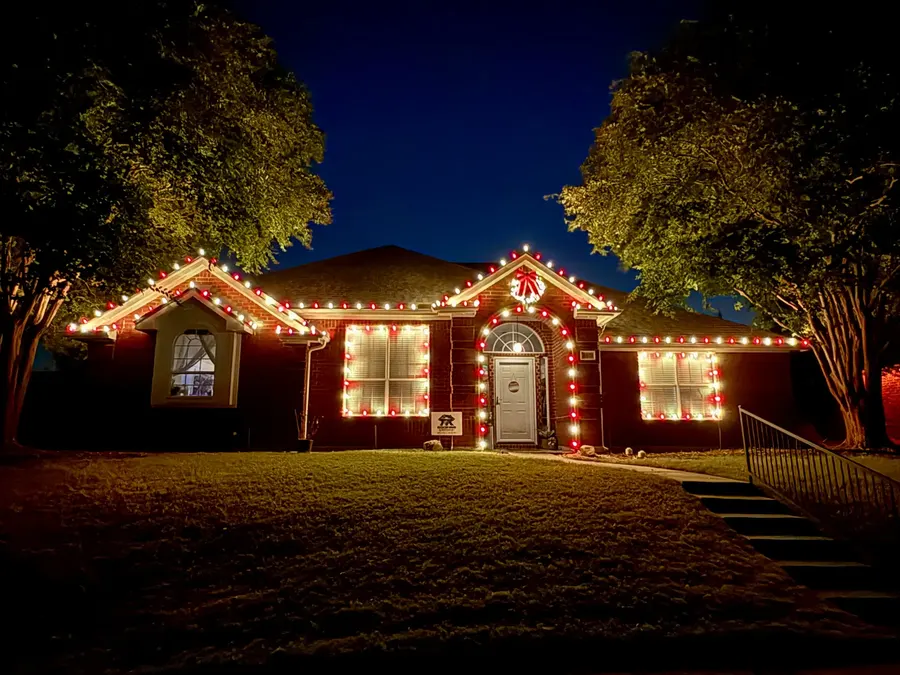 Home at night decorated with red and warm-white holiday lights around the roofline, windows, and front door